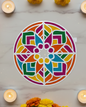 Decorative white cutout with geometric pattern on a marble surface surrounded by candles and flowers.